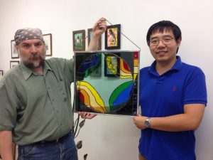 Urii Guchenia, left, and Ran Hong proudly hold up a stained-glass rendering of the magnetic field in the Muon g-2 experiment's storage ring. Photo courtesy of Ran Hong