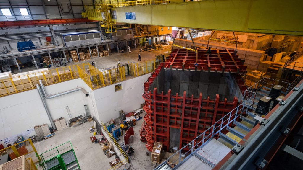The steel cage for one of the two ProtoDUNE detectors is outfitted with a steel top, hoisted into position by a crane. Photo: CERN