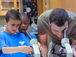 A volunteer helps two visitors use microscopes during science camp. Photo: SciTech Museum