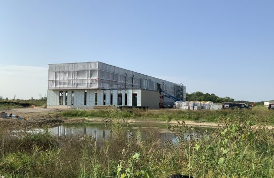 A construction site with a building with an exterior that looks far along in front of a blue sky.