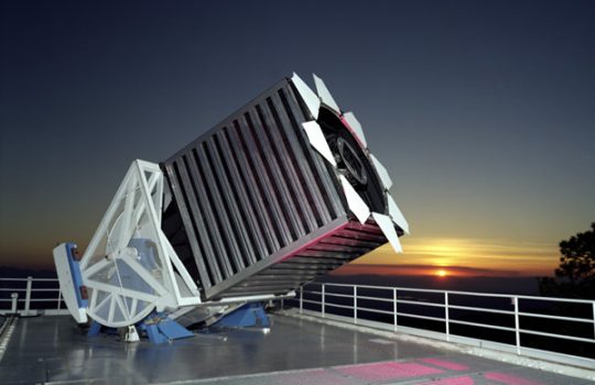 A large telescope on a rooftop, the sunset behind it