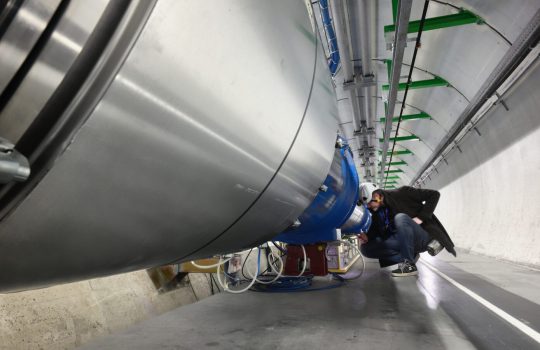 A man kneels to examine a large piece of complex equipment