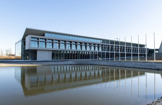 Integrated Engineering Research Center and its reflection in the pond. About ten flag poles and their reflections are also visible.