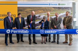 Deputy Secretary of Energy David Turk and Fermilab Director Lia Merminga cut a large ribbon with oversized ceremonial scissors while other people look on