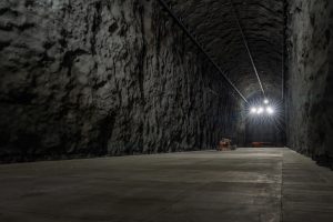 Dimly lit cavern tunnel with lights glowing at the far end