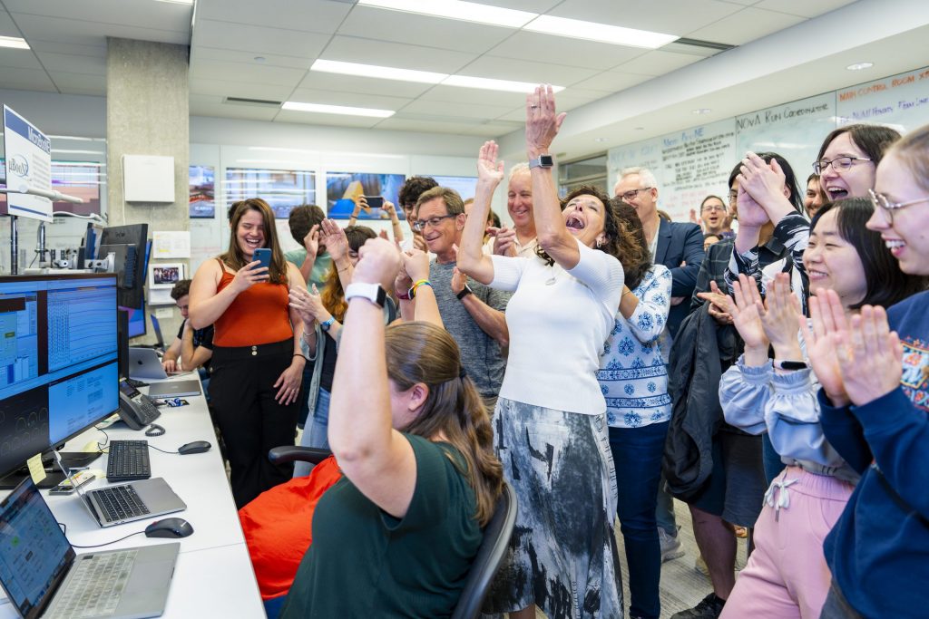 Group of people in a control room celebrating a milestone achievement with joyful expressions, clapping and with raised hands.