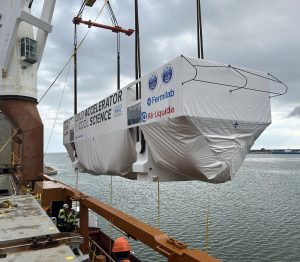 A large box is being transferred from a barge to a ship