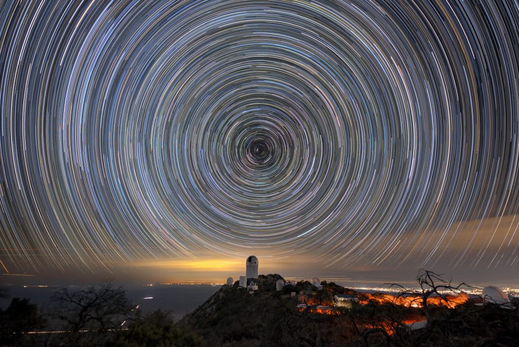 Circles of light on the night sky. A telescope dome atop a mountain is below the center of the circle