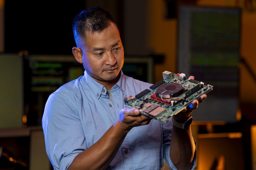 Nhan Tran, head of Fermilab’s AI Coordination division, holds a circuit board used for particle tracker data analysis. Credit: JJ Starr, Fermilab