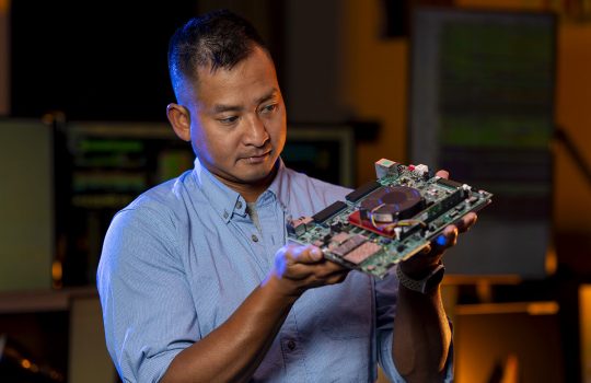Nhan Tran, head of Fermilab’s AI Coordination division, holds a circuit board used for particle tracker data analysis. Credit: JJ Starr, Fermilab