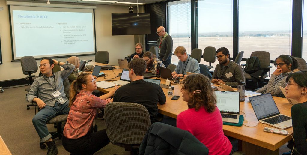 Facilitators Melissa Quinnan, left, and Colin Crovella, center, discuss analysis with students during the 2026 CMS Data Analysis School at Fermilab. Credit: Marguerite Tonjes, UIC