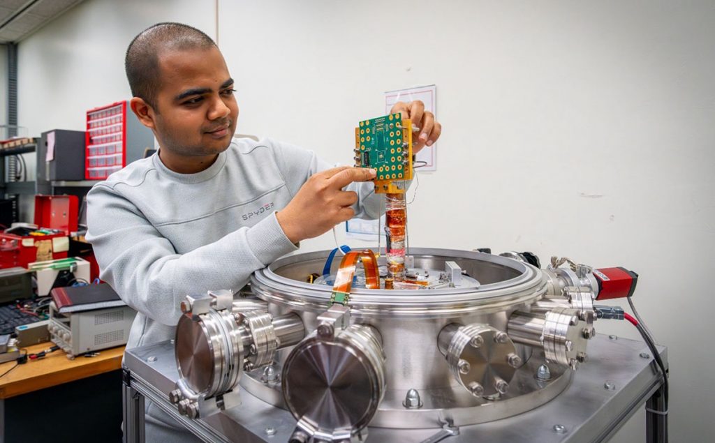 Fermilab engineer Yash Saxena holds a custom circuit board designed to measure chip performance in cryogenic environments. Credit: JJ Starr, Fermilab